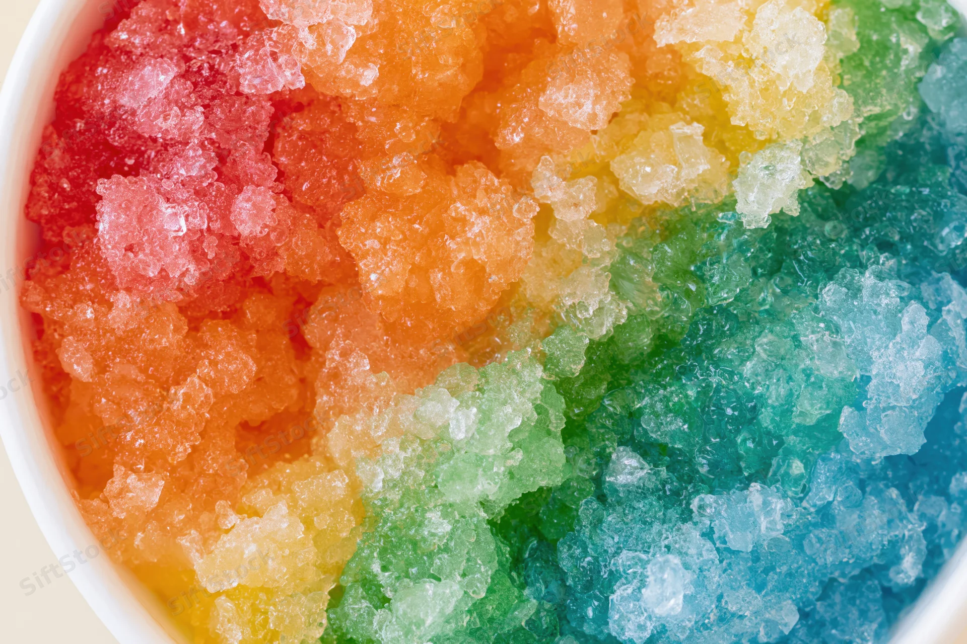 Rainbow shave ice in a white cup viewed from directly overhead
