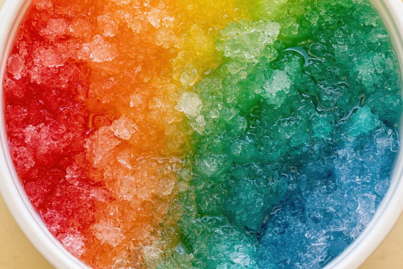 Rainbow shave ice in a white cup viewed from directly overhead