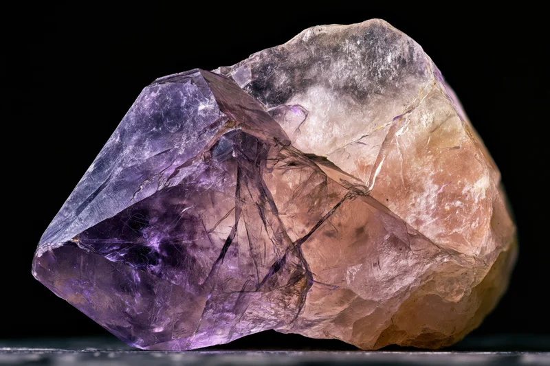 Raw amethyst crystal resting on a flat surface against black background
