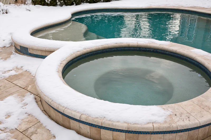 Snow-covered hot tub and swimming pool in a residential backyard