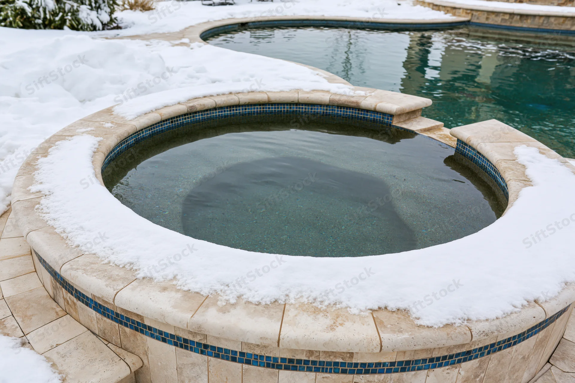 Snow-covered hot tub and swimming pool in a residential backyard
