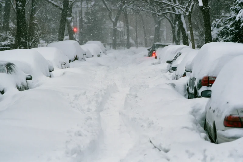 Snow-covered residential street with parked cars during heavy snowstorm