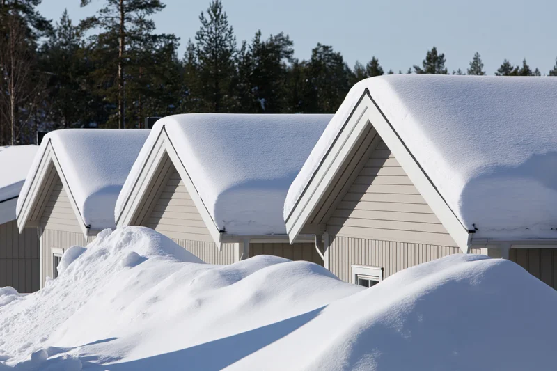 Row of pale grey scandinavian houses with thick snow on roofs and ground in winter landscape