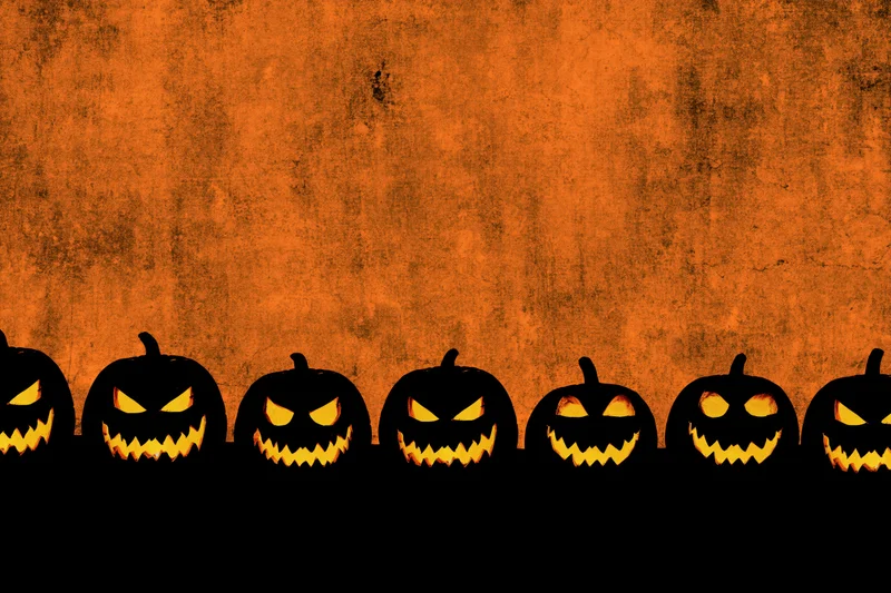 Row of carved jack-o-lantern silhouettes glowing against orange textured background