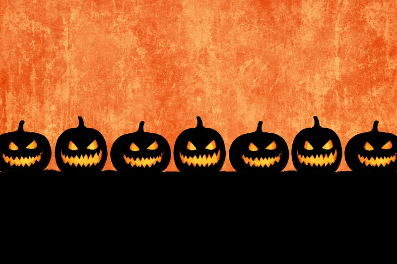 Seven carved jack-o-lantern silhouettes in a row against an orange textured background with black copyspace below