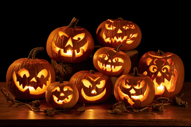 Seven carved jack-o-lanterns glowing with candles on a wooden table at night