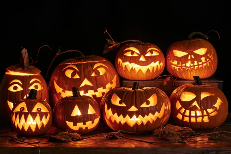 Seven carved jack-o-lanterns glowing with candles on a wooden table at night