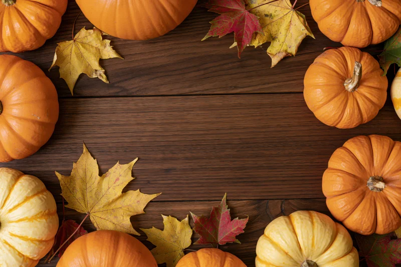 Pumpkins and autumn leaves arranged around a wooden table with central copyspace