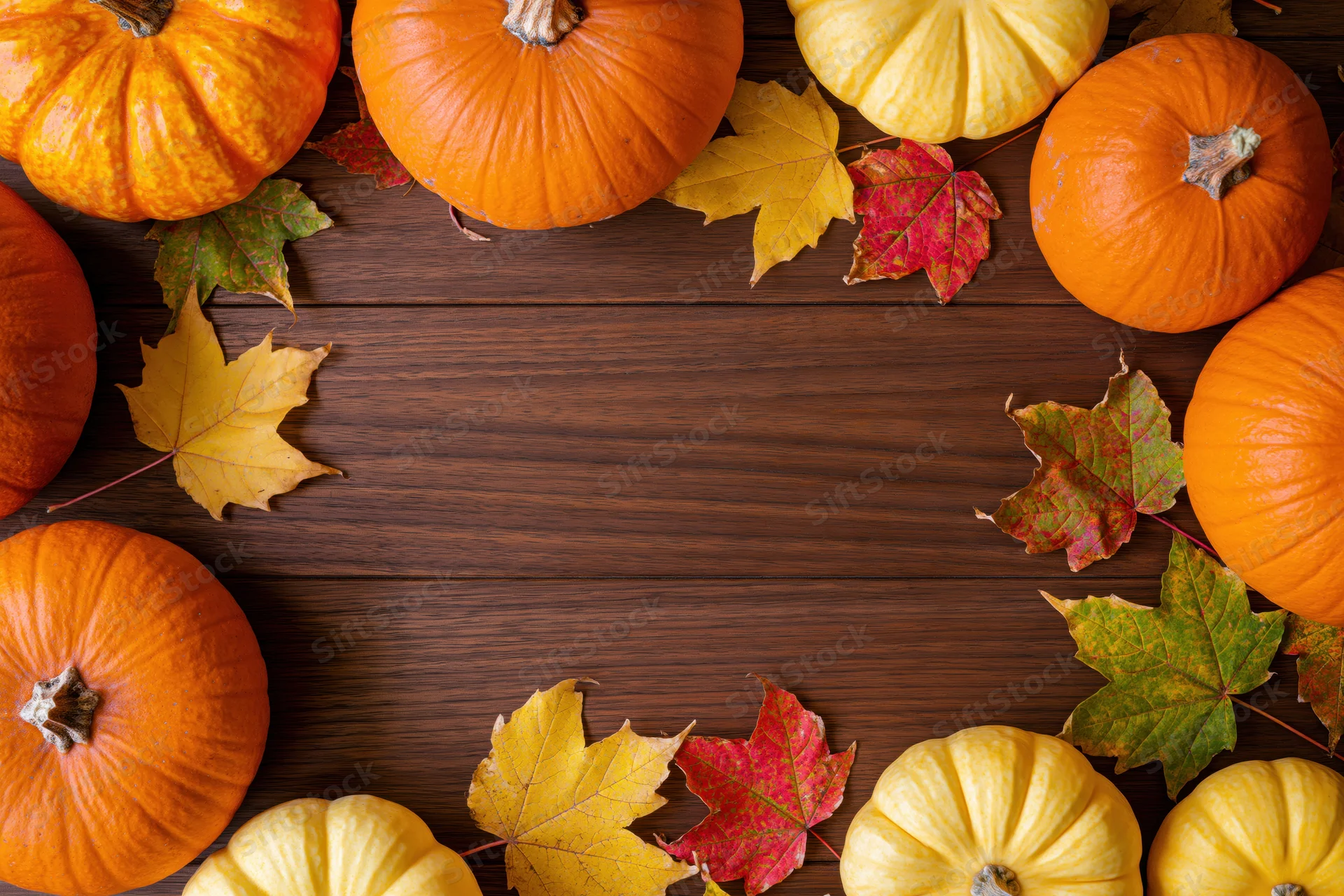 Pumpkins and autumn leaves arranged around a wooden table with central copyspace