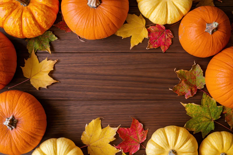 Pumpkins and autumn leaves arranged around a wooden table with central copyspace