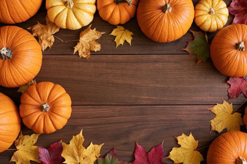 Pumpkins and autumn leaves arranged in a border around a wooden table with copyspace in the center