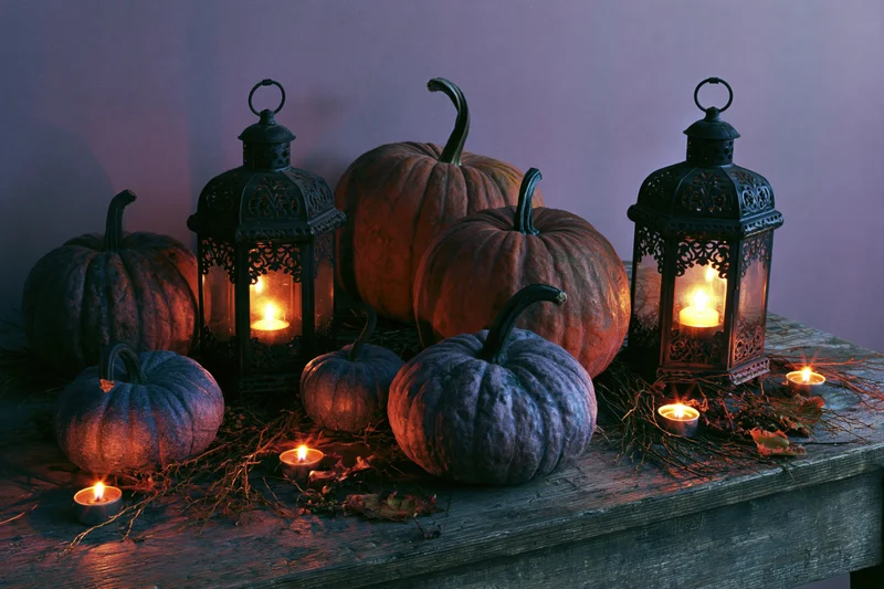 Pumpkins and lanterns with candles arranged on a rustic wooden table for halloween decoration
