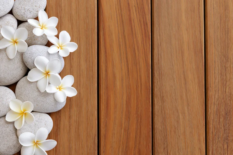 Smooth stones and white plumeria flowers arranged along the left edge of a wooden deck, leaving copyspace on the right