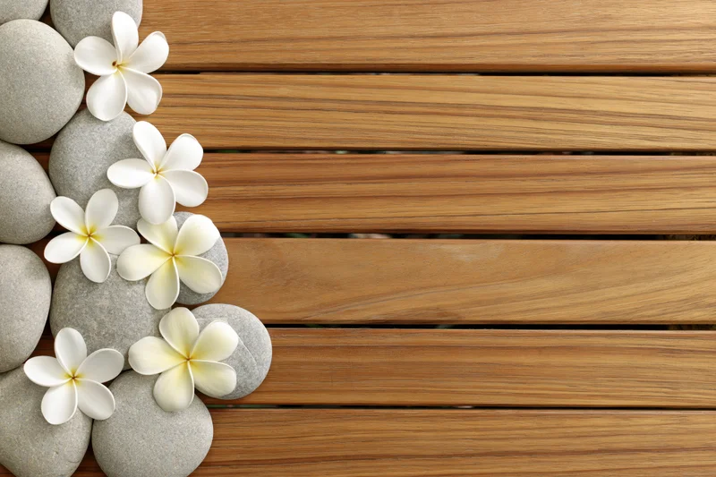 Smooth stones and white plumeria flowers arranged on wooden deck surface