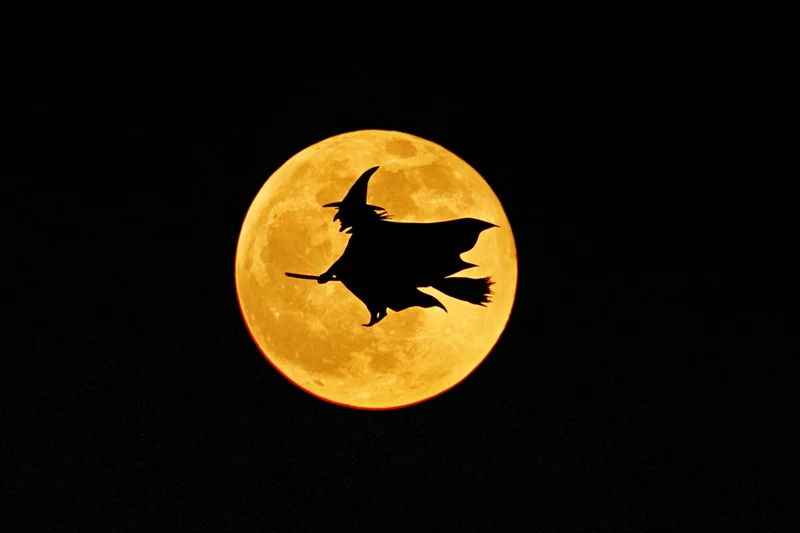Silhouette of a witch riding a broomstick against a full orange moon at night