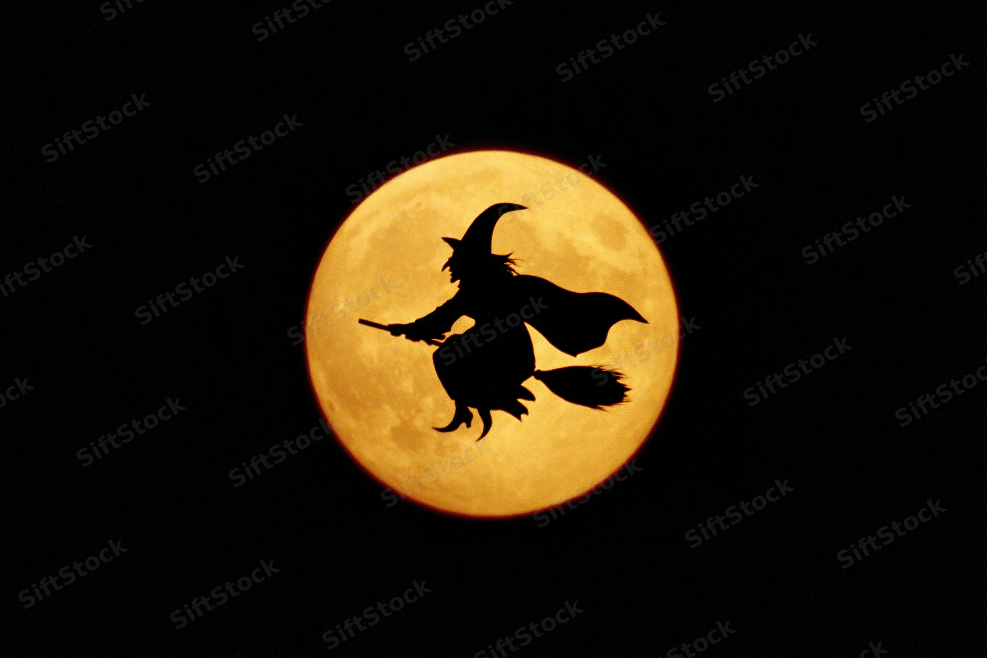 Silhouette of a witch riding a broomstick against a full moon at night