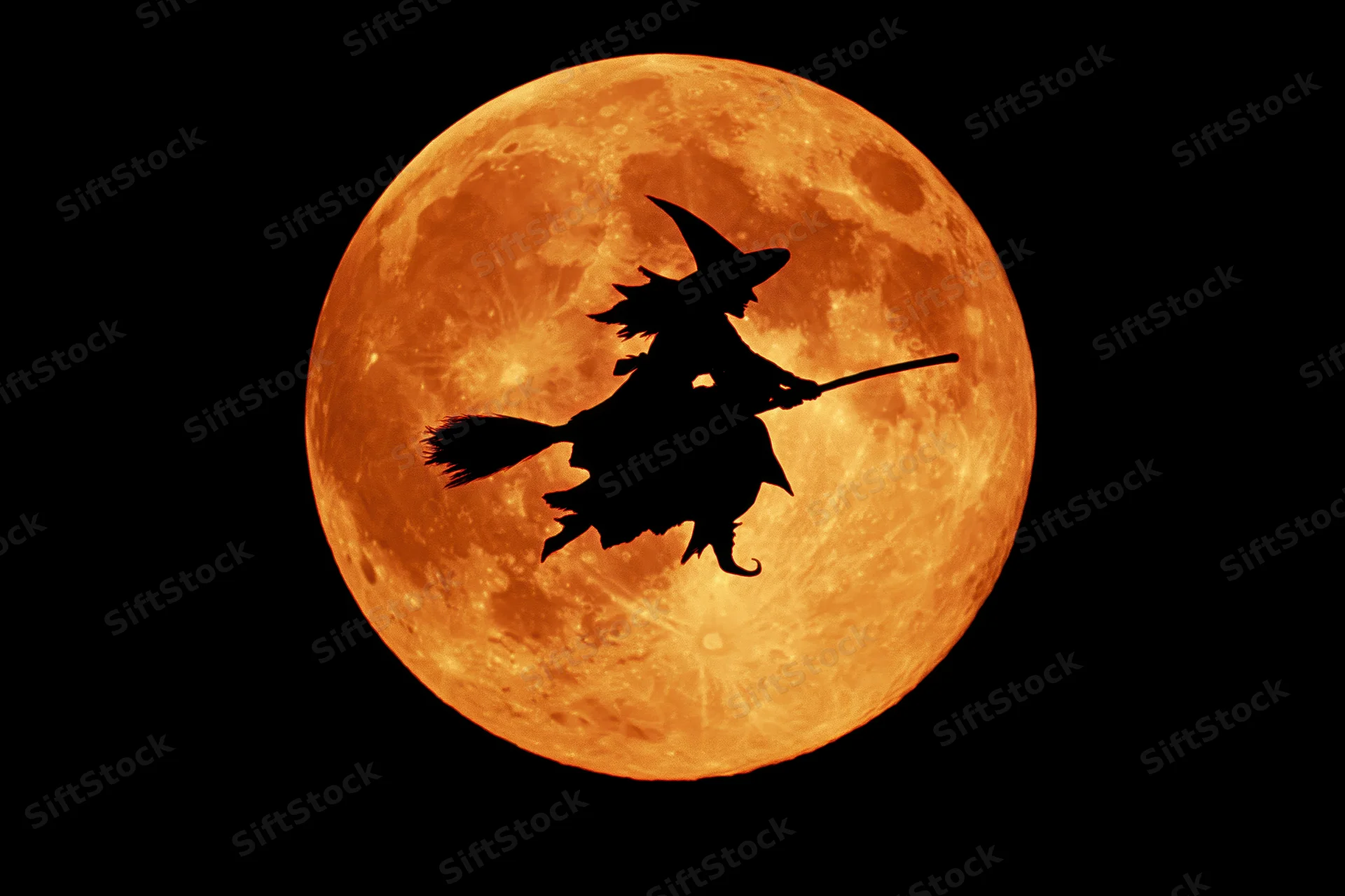 Silhouette of a witch riding a broomstick in flight against an orange full moon at night