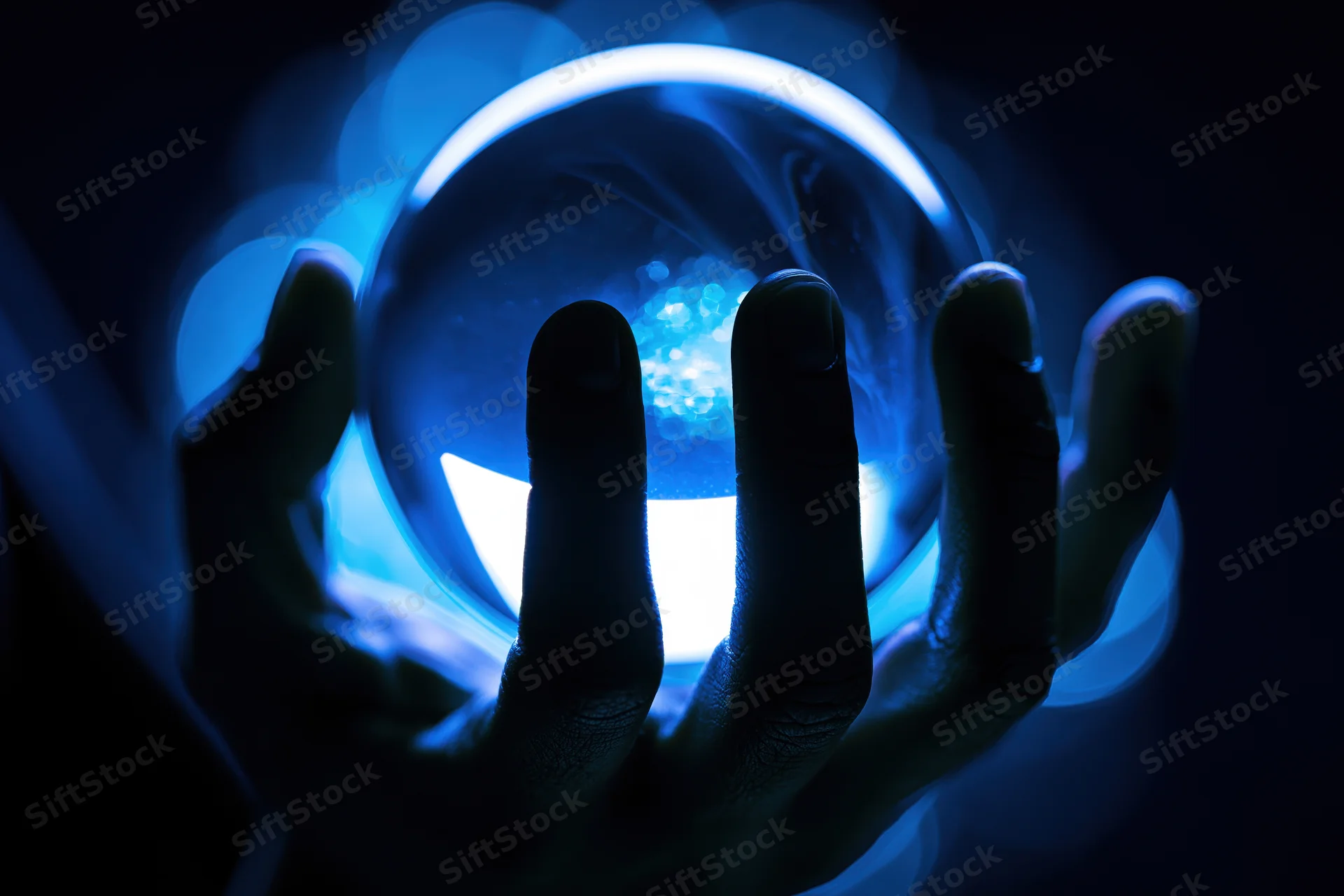 Silhouetted hands holding a glowing blue crystal ball in darkness