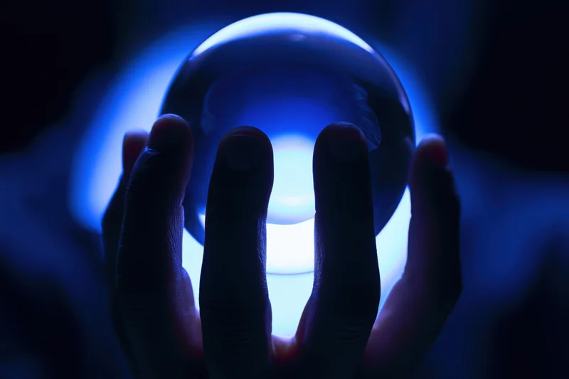 Silhouetted hands holding a glowing blue crystal ball against dark background