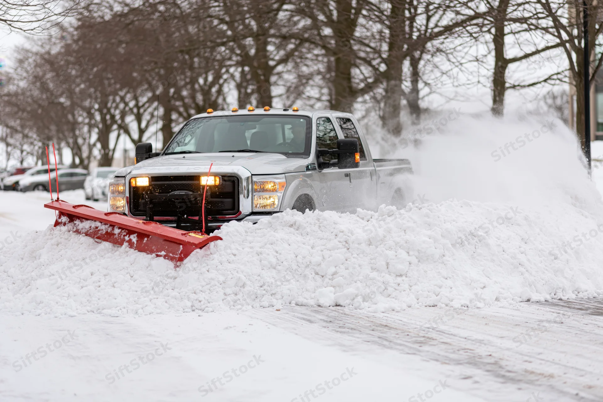 Silver heavy-duty pickup truck with red snow plow clearing snow on a street