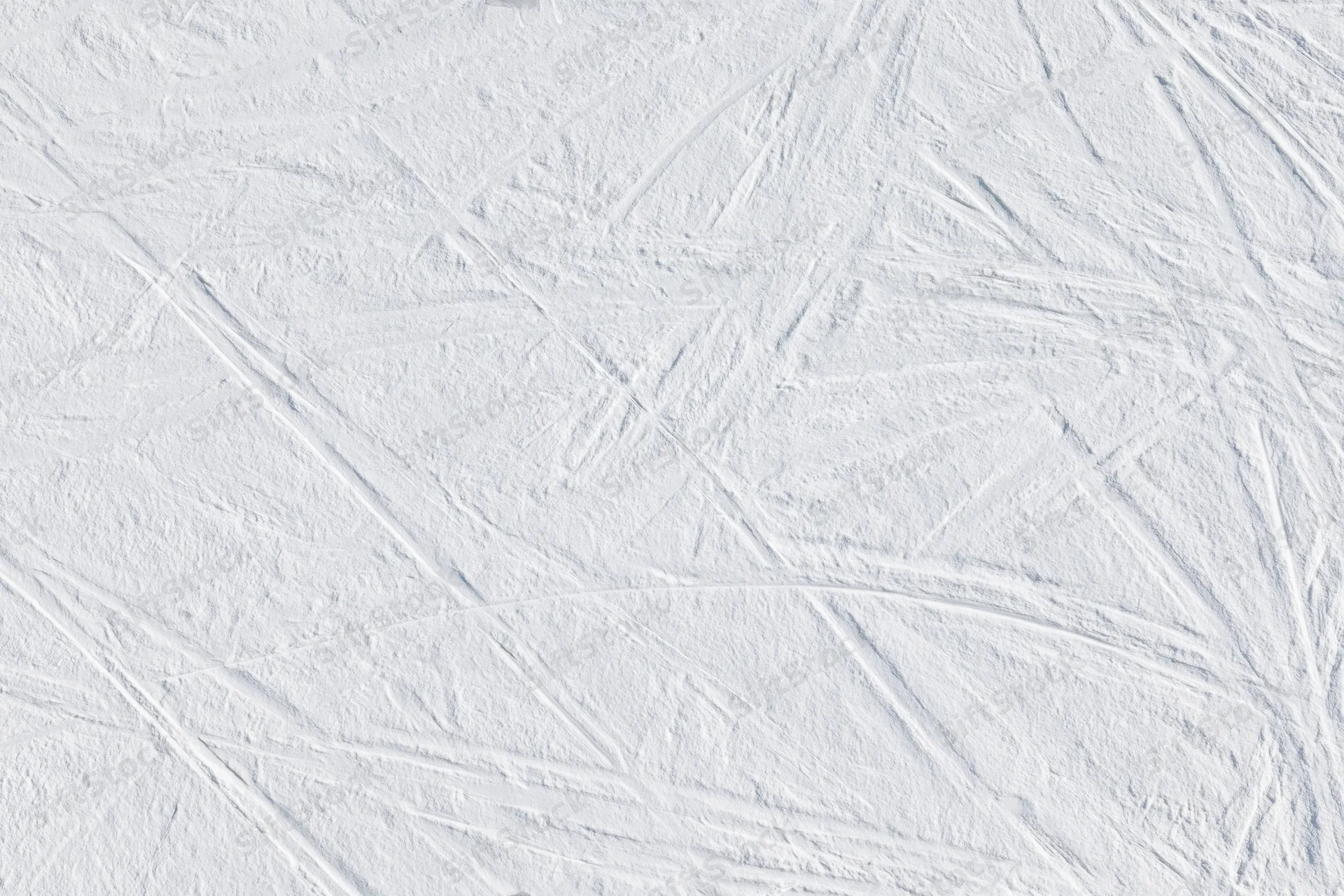 Snow-covered ski slope with overlapping carved ski tracks across the surface