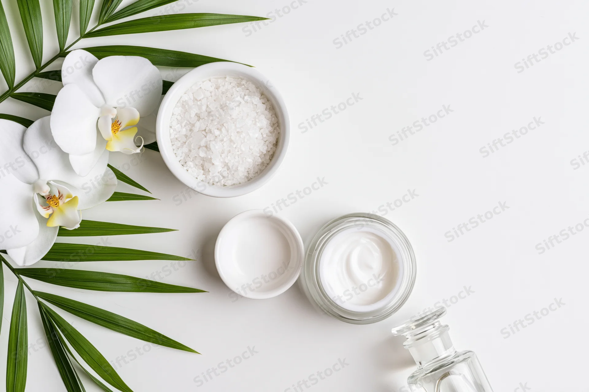 Skincare products and tropical flowers arranged on a white surface with copy space