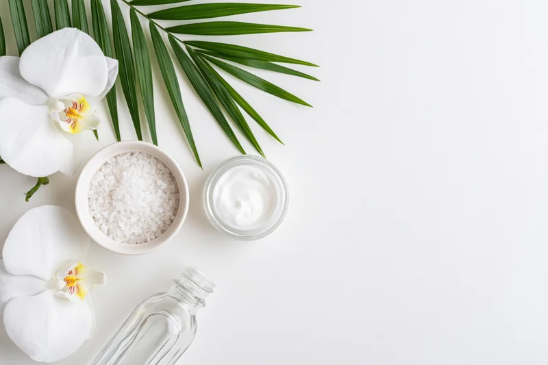 Skincare products and tropical flowers arranged on white surface with copyspace