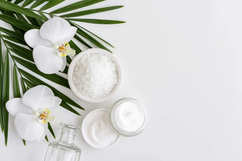 Skincare products arranged with white orchids and palm leaves on a white surface