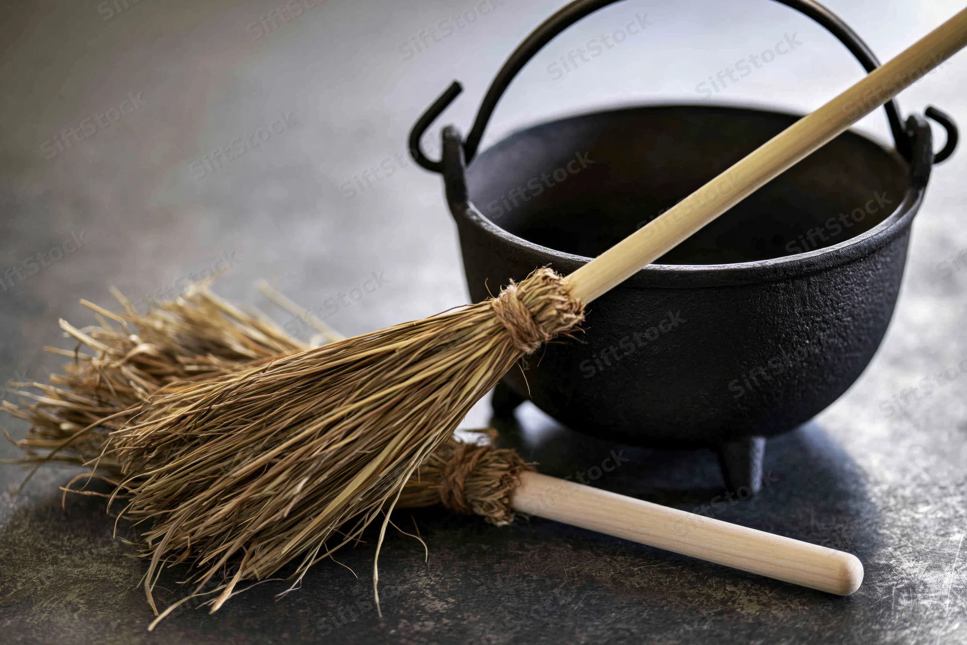 Small black cast iron cauldron with a broom resting beside it on a dark textured surface