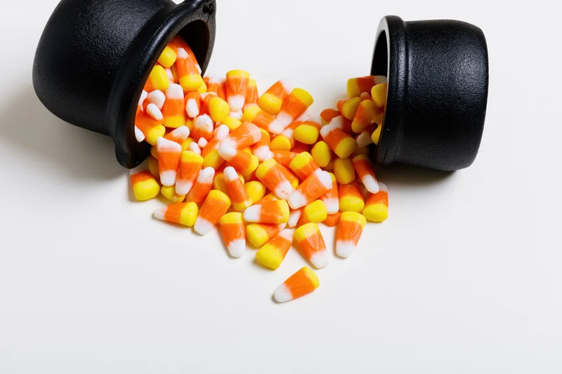 Candy corn spilled from black ceramic witch cauldrons on white surface