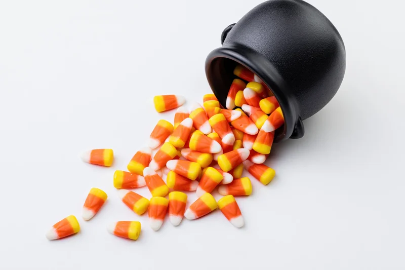 Candy corn spilled from a black ceramic cauldron on white background