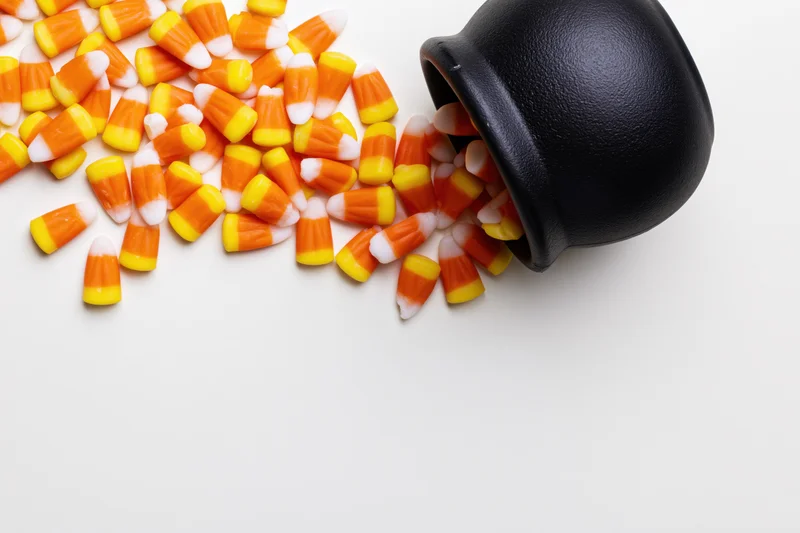 Candy corn spilled from a black witch cauldron on white background