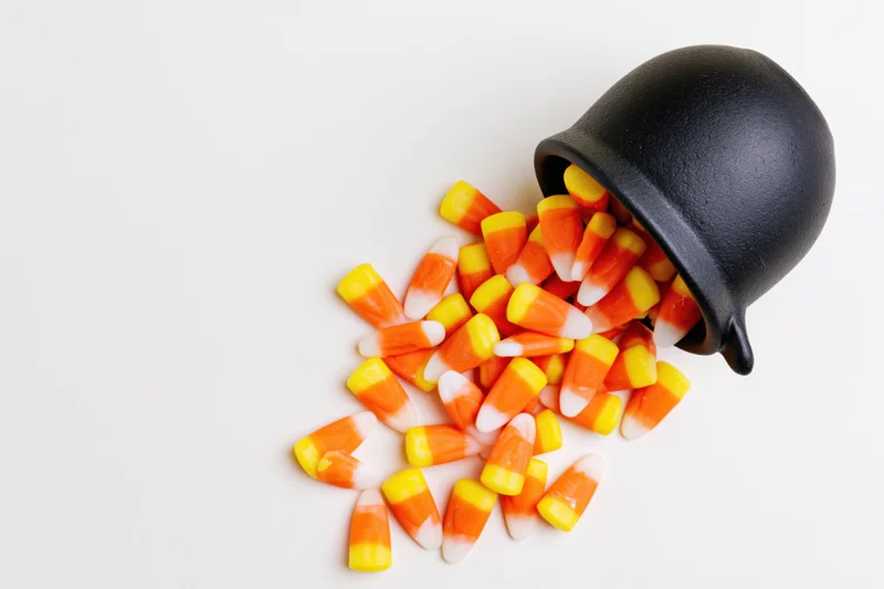 Candy corn spilled from a black ceramic cauldron on white background