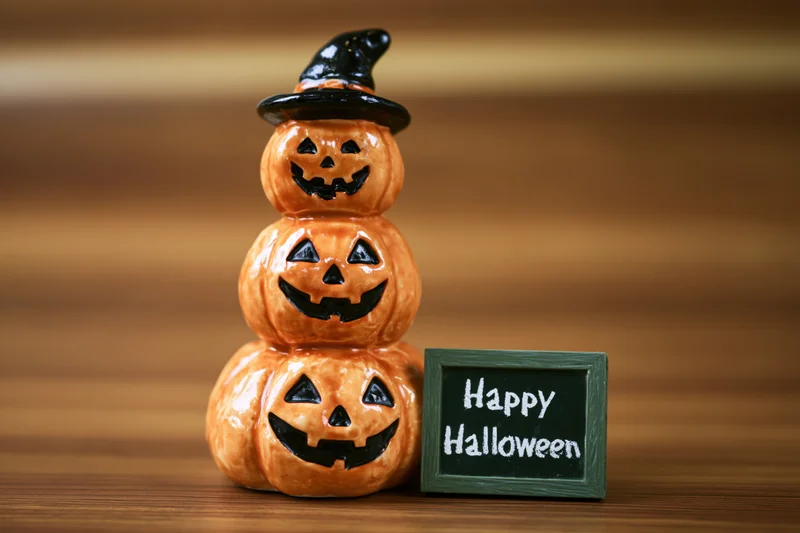 Stacked ceramic pumpkins with witch hat and happy halloween sign on wooden table