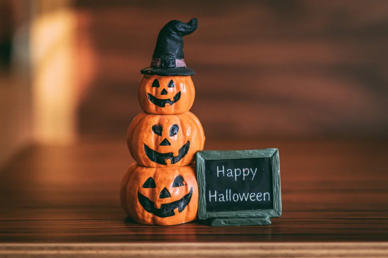 Stacked ceramic pumpkins with witch hat and happy halloween sign on wooden table