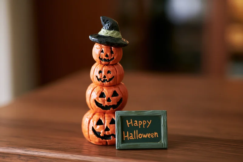 Stacked ceramic pumpkins with witch hat and happy halloween sign on wooden table
