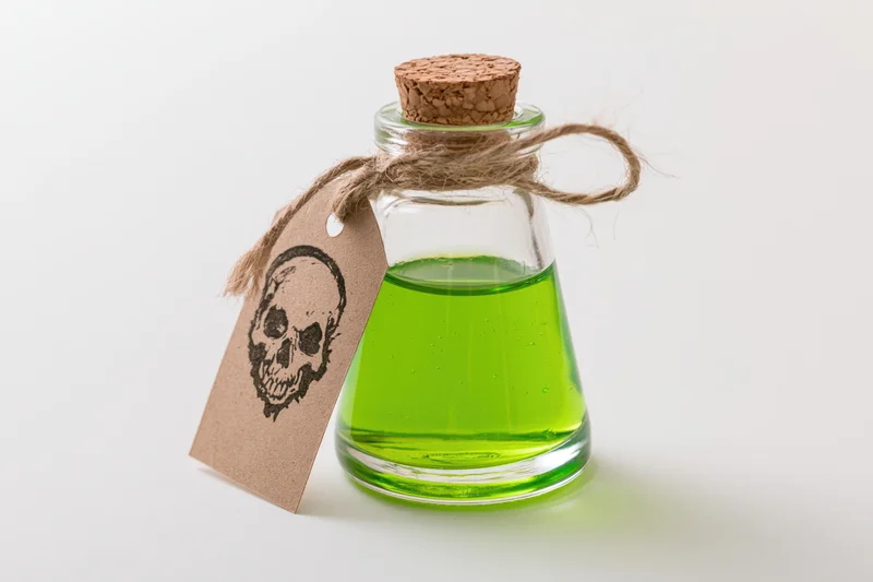 Small glass bottle filled with bright green liquid and skull tag on white background