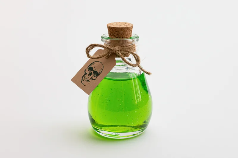Small clear glass bottle filled with bright green liquid and skull tag on white background