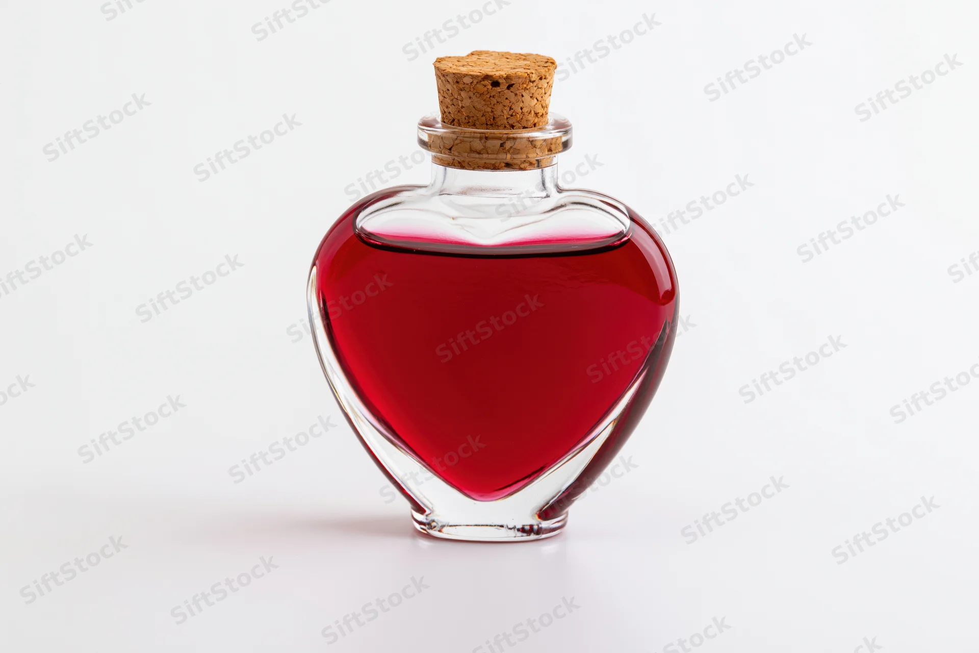 Heart-shaped glass bottle filled with red liquid and cork stopper on white background