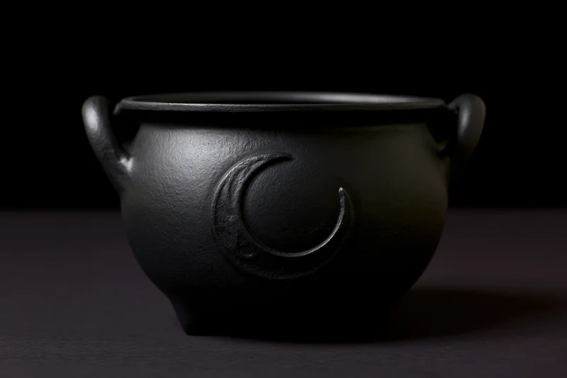 Small matte black cast iron cauldron with crescent moon symbol and side handles on dark surface