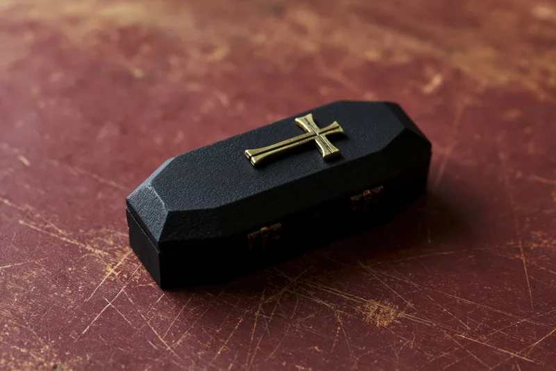 Miniature black coffin model with brass cross on textured red surface