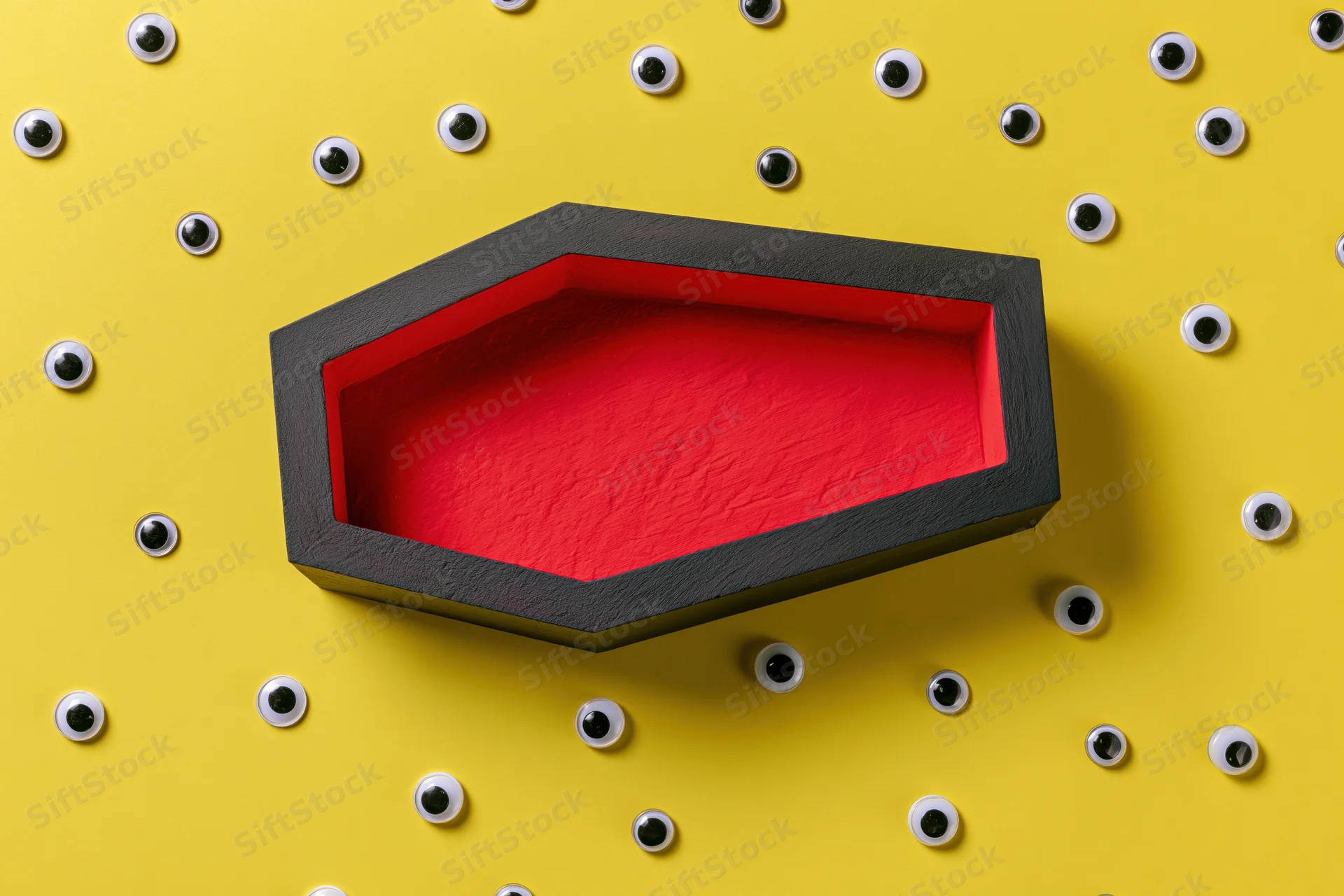 Open coffin prop with red interior on yellow background surrounded by googly eyes