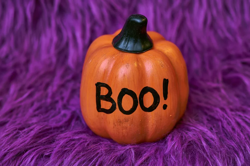 Small orange ceramic pumpkin with boo painted in black lettering on purple furry surface