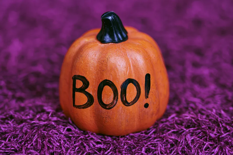 Small orange ceramic pumpkin with boo painted in black lettering on purple textured surface