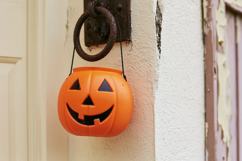 Orange plastic jack-o-lantern candy bucket hanging on a door ring outside a house