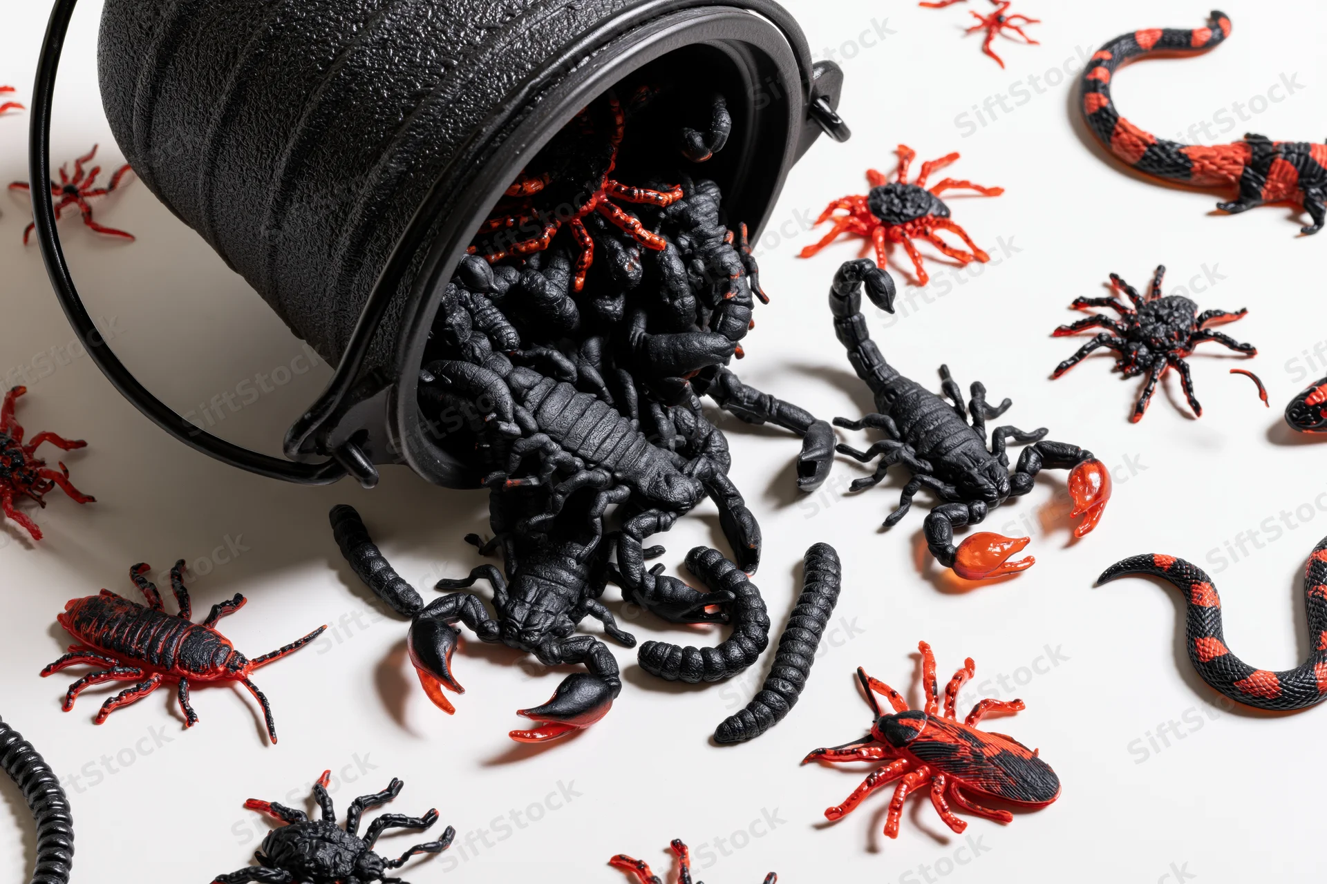 Black bucket tipped over spilling plastic scorpions spiders and snakes on white surface
