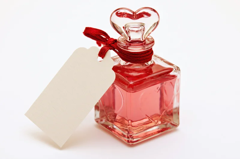 Small square glass perfume bottle with heart-shaped cap and blank tag tied with red string on white background