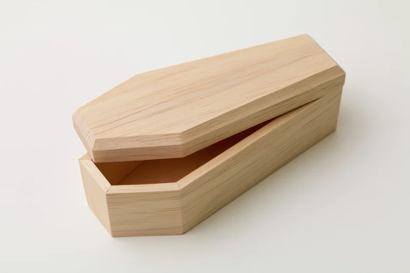 Small unfinished wooden miniature coffin box with lid slightly open on white background