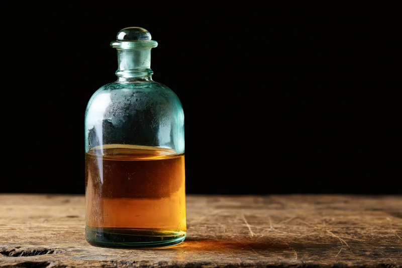 Vintage apothecary glass bottle with amber liquid on wooden surface against black background
