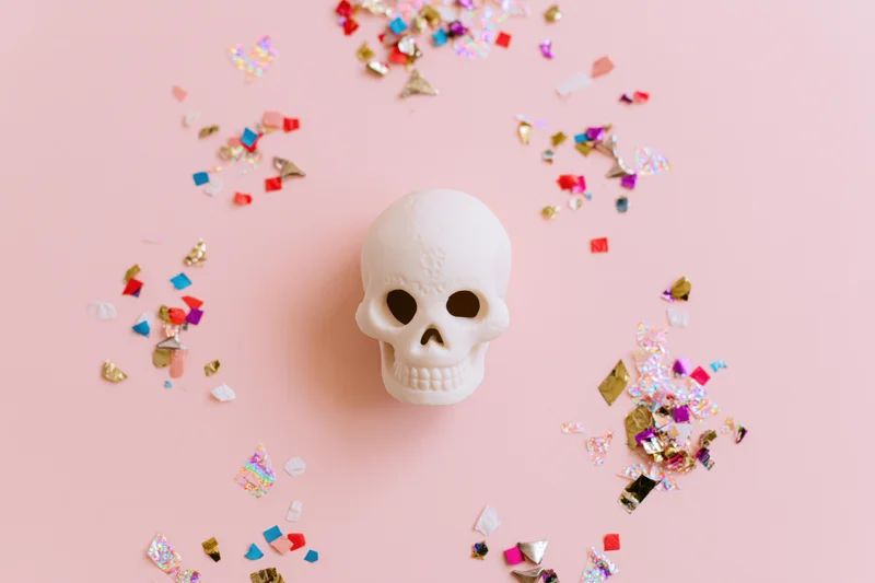 White ceramic sugar skull figurine centered on pink surface surrounded by colorful confetti